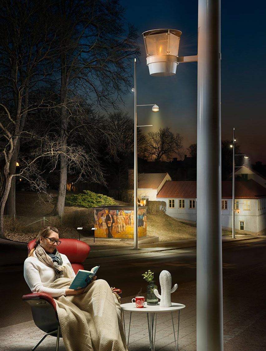 Kvinna sitter i en fotölj och läser ute på gatan under en belysningsstolpe