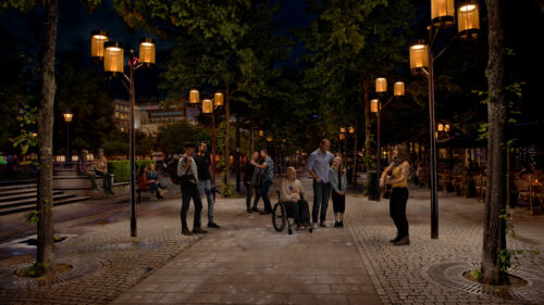 En trubadur spelar vid en lyktstolpe från Moramast i Kungsträdgården, Stockholm, medan folk lyssnar och dansar.