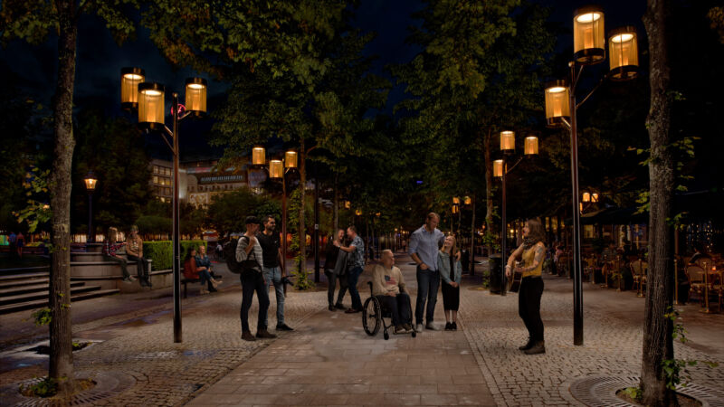 En trubadur spelar vid en lyktstolpe från Moramast i Kungsträdgården, Stockholm, medan folk lyssnar och dansar.